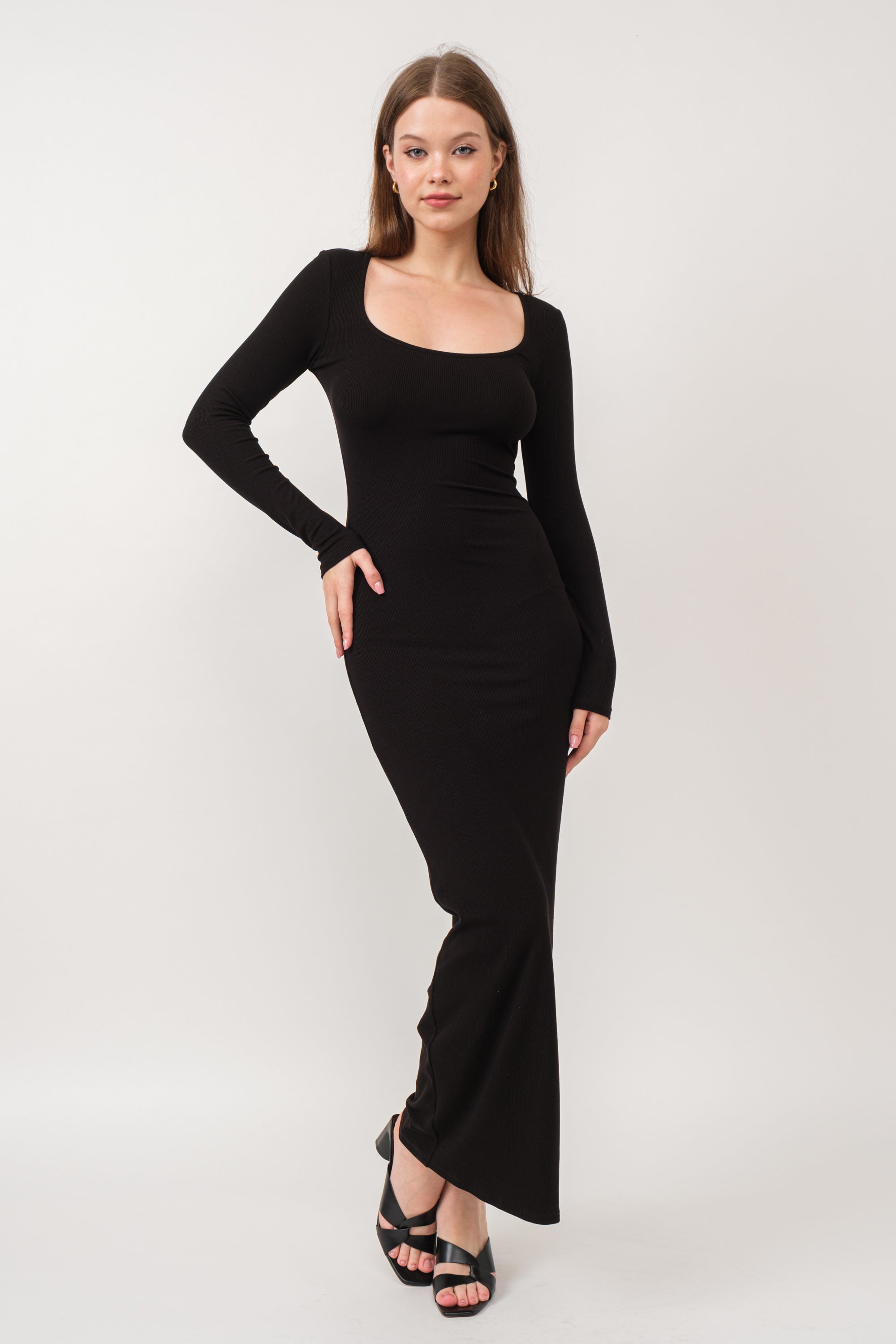 A model wearing a black ribbed maxi dress against a white wall.