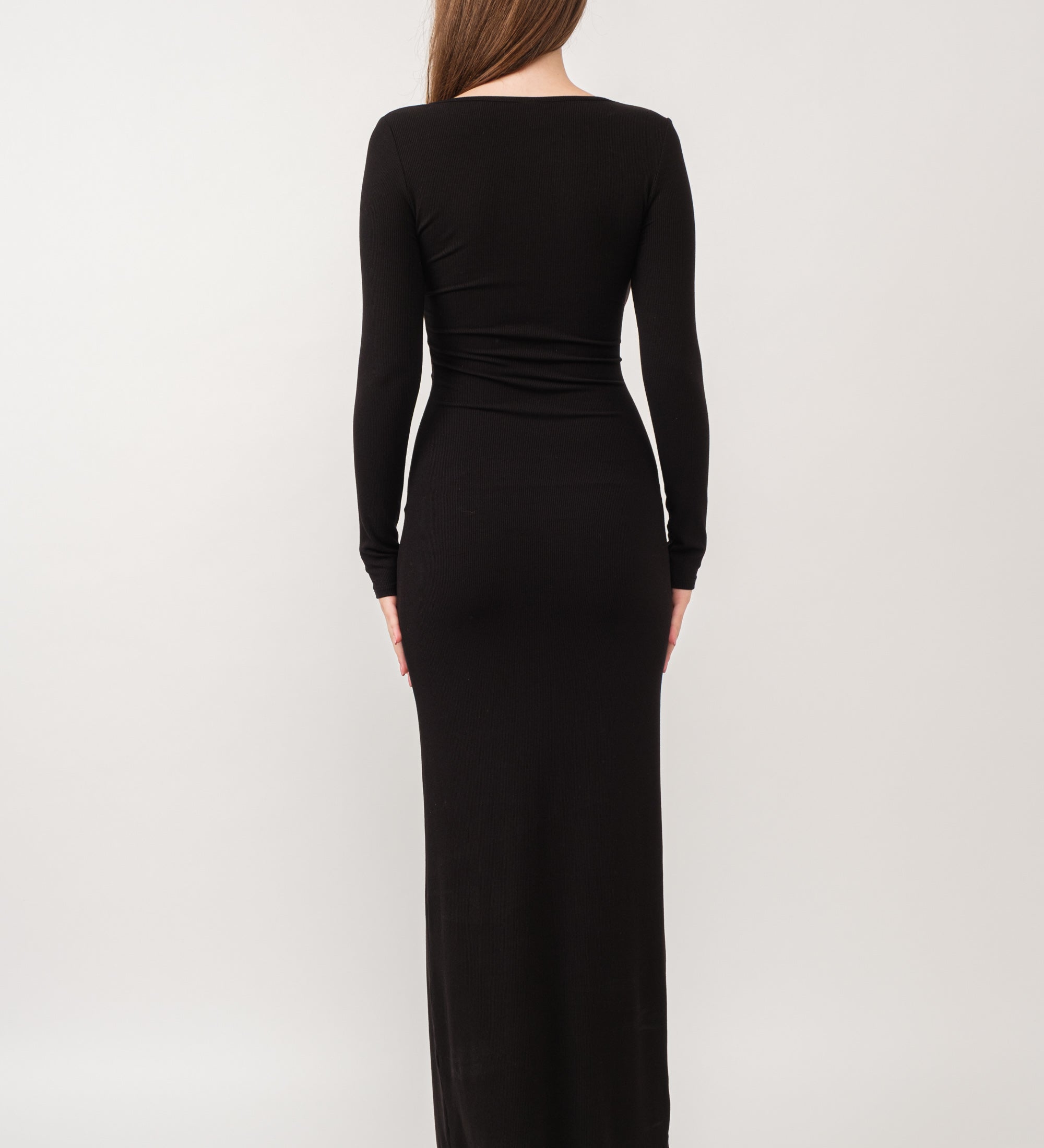A model wearing a black ribbed maxi dress against a white wall. 