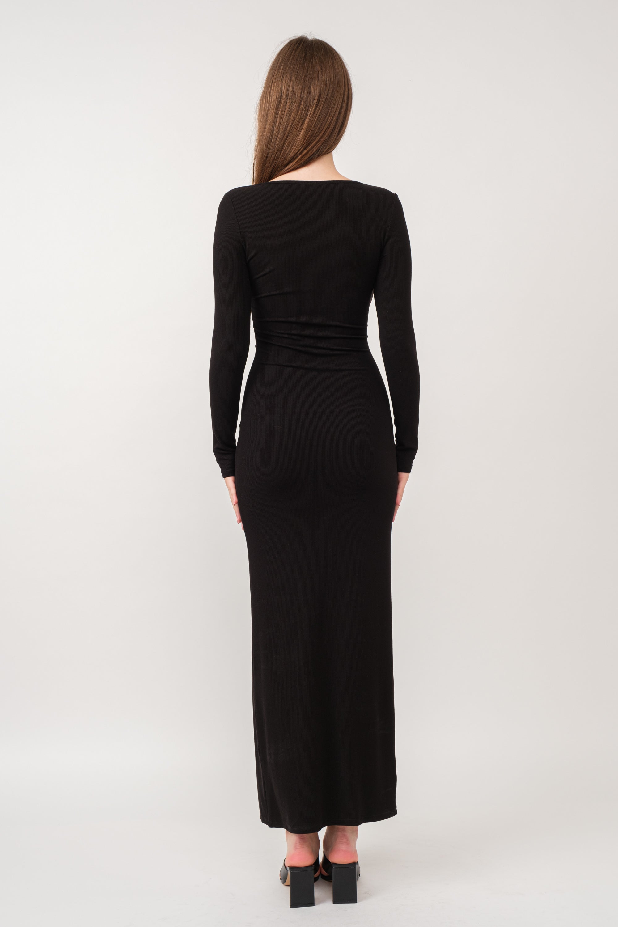 A model wearing a black ribbed maxi dress against a white wall.