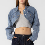 A model wearing a cropped denim jacket against a white wall.