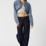 A model wearing a cropped denim jacket full body image against a white wall.