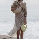 A model wearing two straw woven handbags while standing on the beach