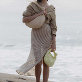 A model wearing two straw woven handbags while standing on the beach