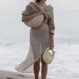 A model wearing two straw woven handbags with knot handles while standing on the beach