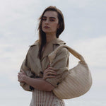 A model wearing a natural straw woven shoulder bag with a knot handle while standing outisde