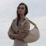 A model wearing a large straw woven shoulder bag with a knot handle while standing outside