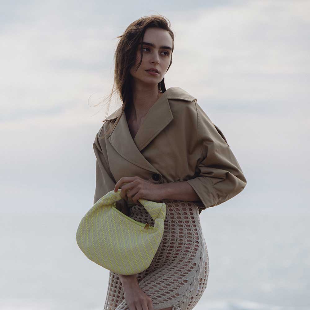 A model wearing a small yellow straw woven top handle bag with a knot handle