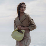 A model wearing a small yellow straw woven top handle bag with a knot handle while standing outside