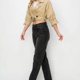 A model wearing a cropped trench jacket sideview full body image against a white wall. 