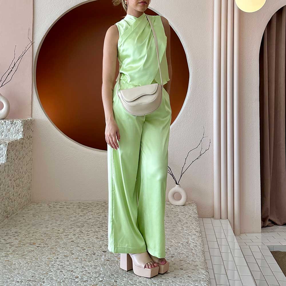 A model wearing a nude vegan leather crossbody bag with a wavy front flap closure.
