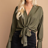 A model wearing a green tie front top against a tan wall.