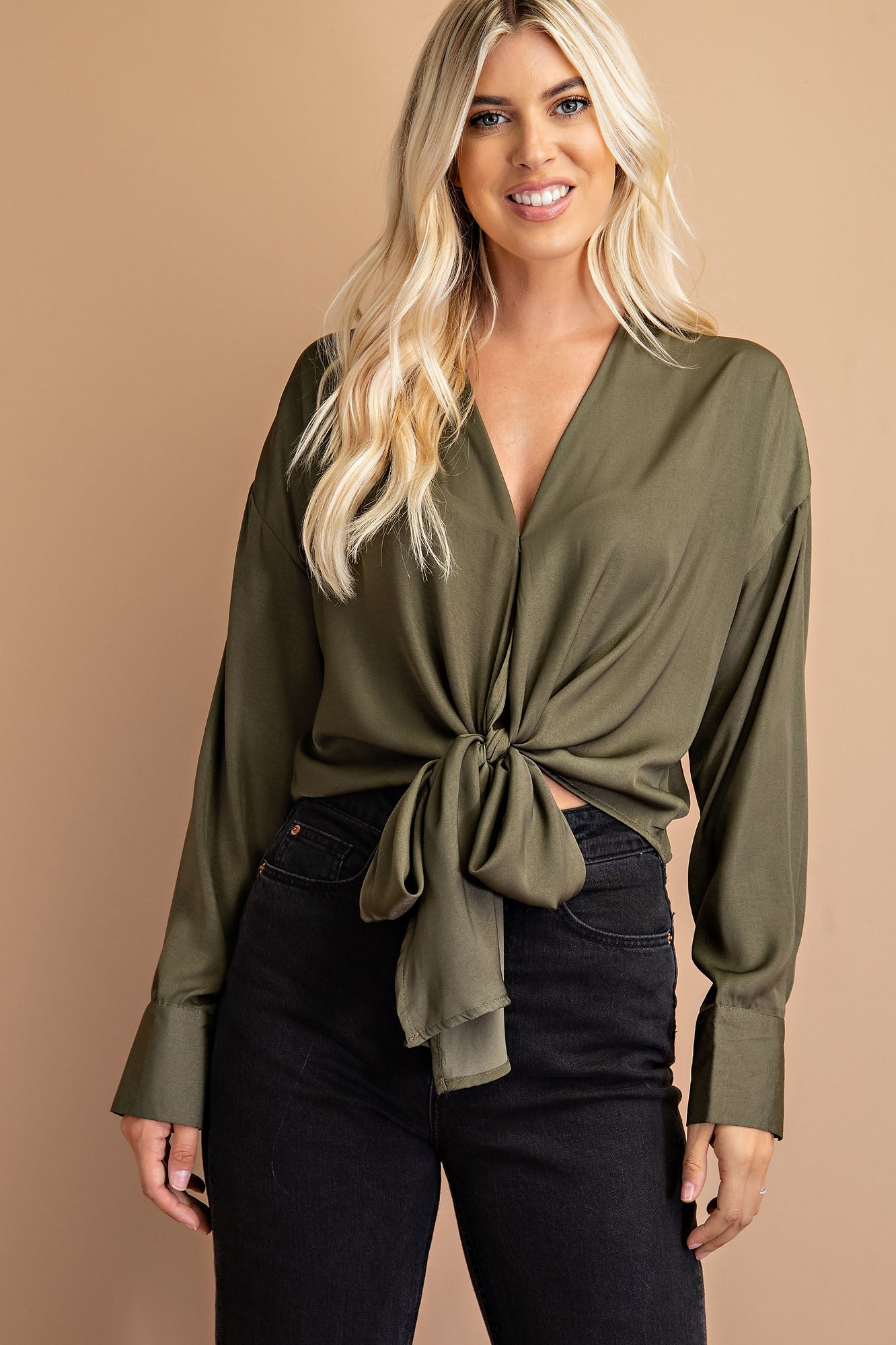 A model wearing a green tie front top against a tan wall.