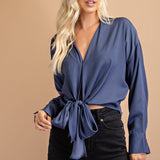 A model wearing a blue tie front top against a tan wall.