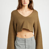 A model wearing a v-neck cropped green sweater against a white background. 