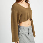 A model wearing a v-neck cropped green sweater against a white wall.