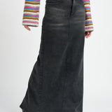 A model wearing a long black denim pencil skirt against a white wall. 