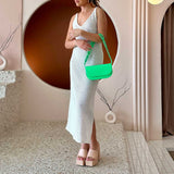 A model wearing a neon green vegan leather shoulder bag with a scalloped strap.