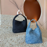 A still image of two large denim woven shoulder bags with zip pouches inside laying against a stone background