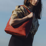 A model wearing a large red woven shoulder bag with a zip pouch while standing outside