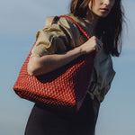 A model wearing a large red vegan leather shoulder bag with a zip pouch inside while standing outisde
