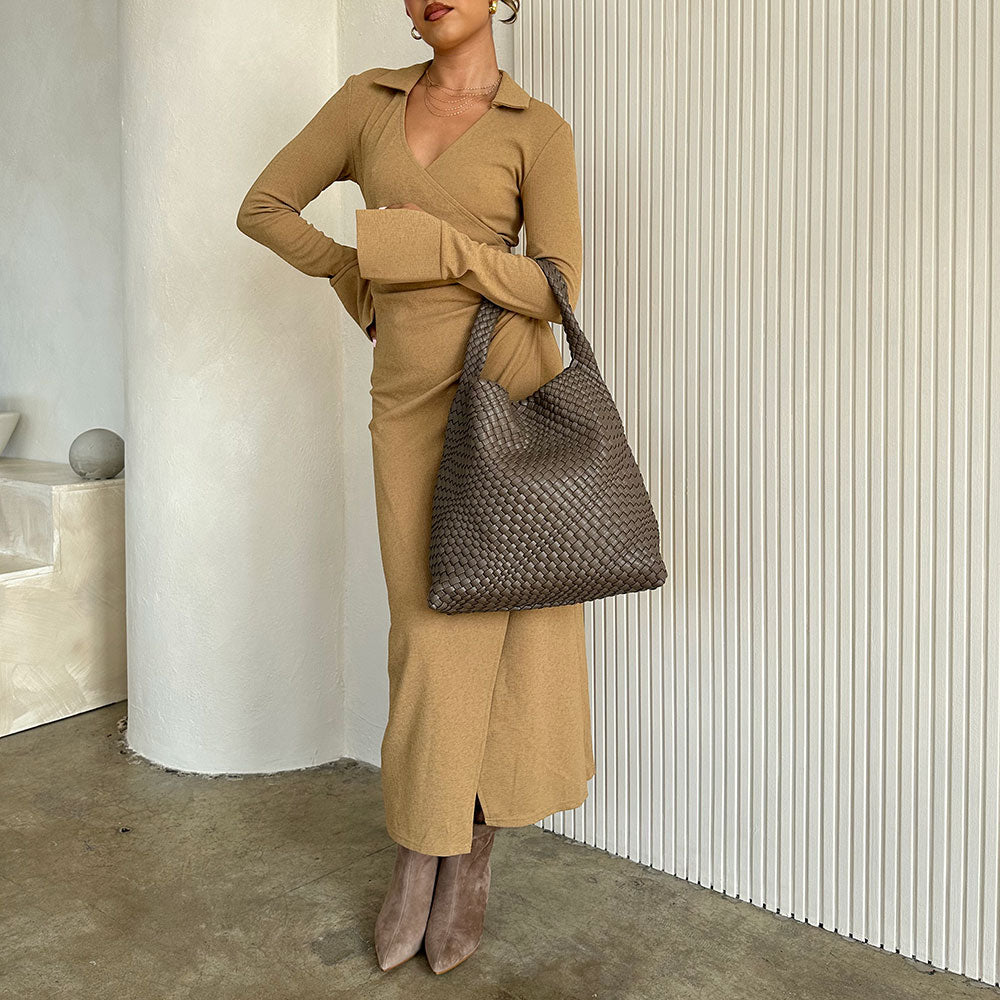 A model wearing a large woven vegan leather shoulder bag against a white wall.
