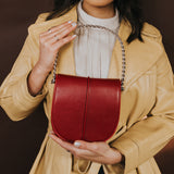 A model holding a red vegan leather crossbody handbag with a yellow jacket on.
