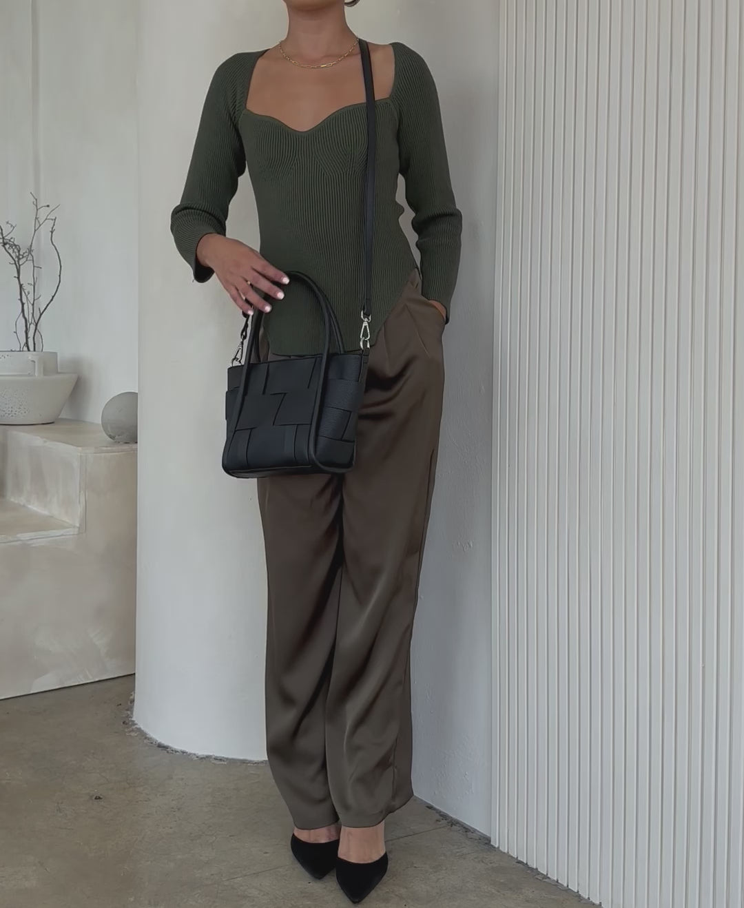 A model wearing a small woven wide strap tote bag against a white wall.