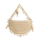 A small natural crochet straw top handle bag with seashell details along the handle.