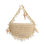 A small natural crochet straw top handle bag with seashell details along the handle