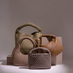A still image of four different woven vegan leather bags against a brown wall and tan props.