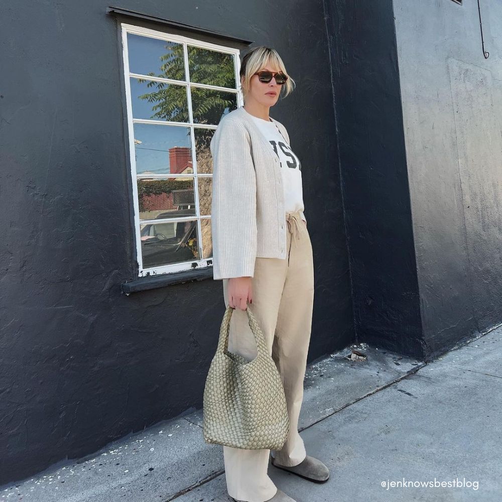 A model wearing a large woven vegan leather shoulder bag against a black wall. 