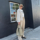 A model wearing a large woven vegan leather shoulder bag against a black wall. 