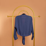 A still image of a blue tie front top on a hanger. Backside view. 