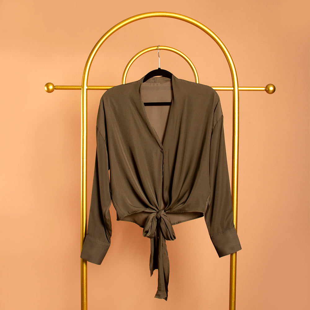 A still image of a green tie front top on a hanger against a orange background.