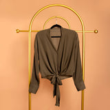 A still image of a green tie front top on a hanger against a orange background.