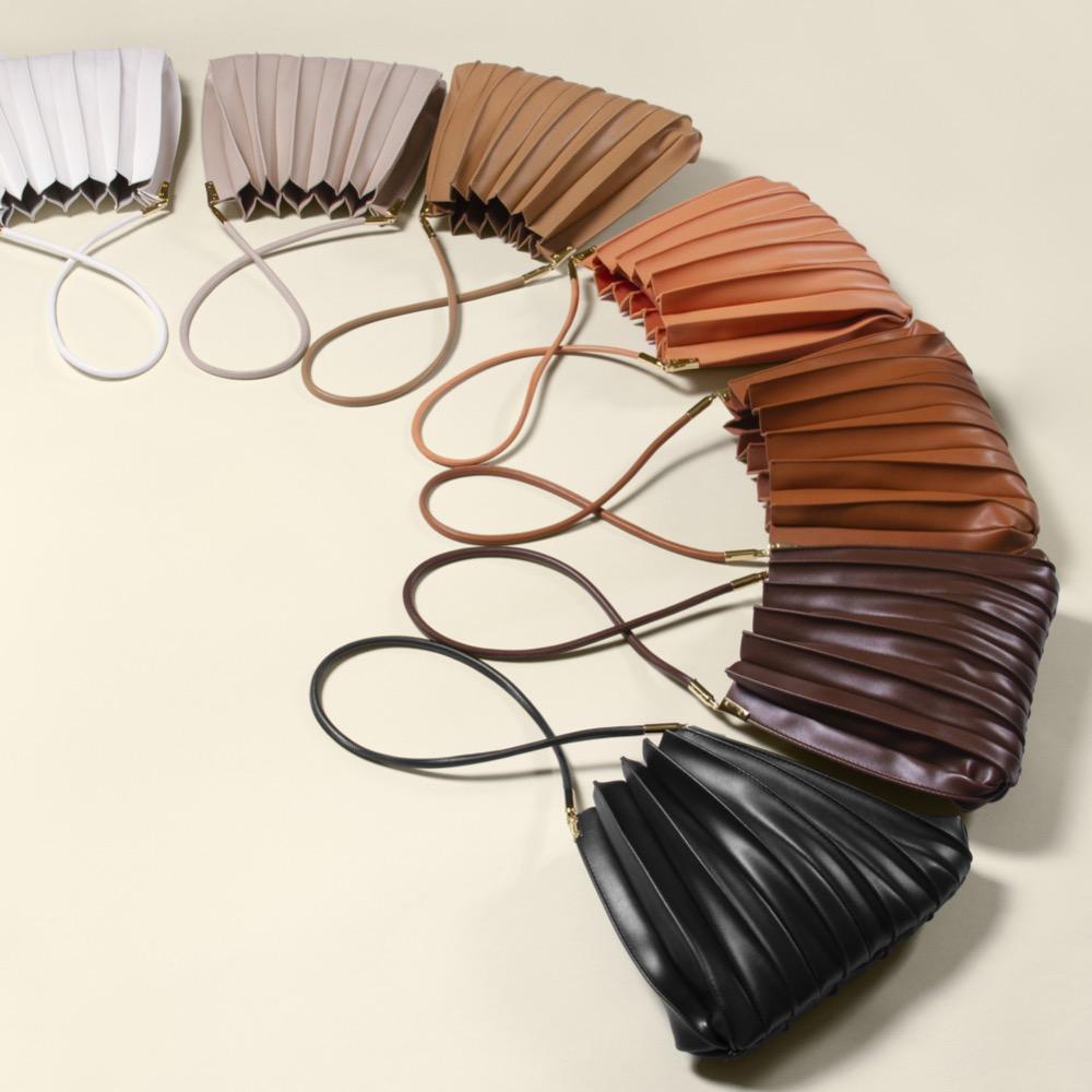 An array of colors of pleated vegan leather shoulder bags laying on the ground. 
