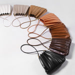 Array of colors of pleated vegan leather shoulder bags laying on the ground.