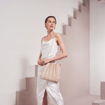 Model wearing a bone pleated vegan leather shoulder bag with a stair design background.