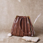 A still photo of a pleated chocolate vegan leather shoulder bag with stones and grass decoration. 