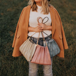 Model holding 3 pleated vegan leather shoulder bags in the grass.