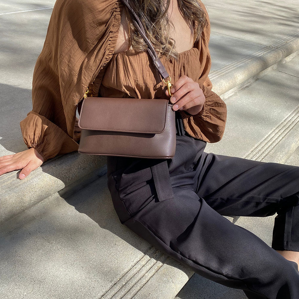 A model wearing a woven crop top and shrug set while sitting on stairs. 