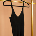 A detail image of a black rib-knit tank top on a hanger against an orange wall.