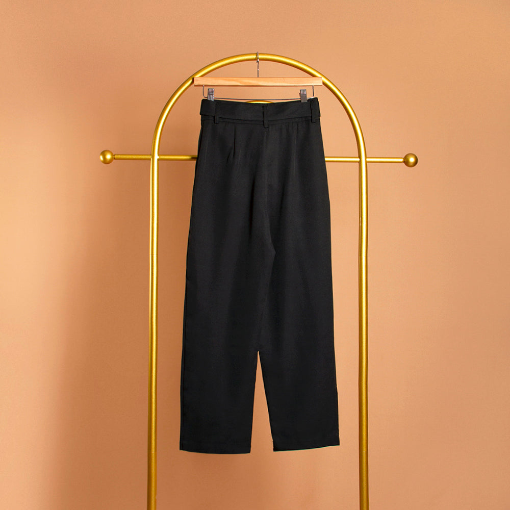 A still image of a black straight leg pant with a belt on a hanger against an orange background. 