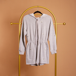 A still image of a grey terry hooded romper on a hanger against a orange wall.