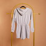 A grey terry hooded romper on a hanger against an orange wall.