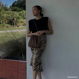 Model wearing a chocolate pleated vegan leather shoulder bag against a white wall outside. 