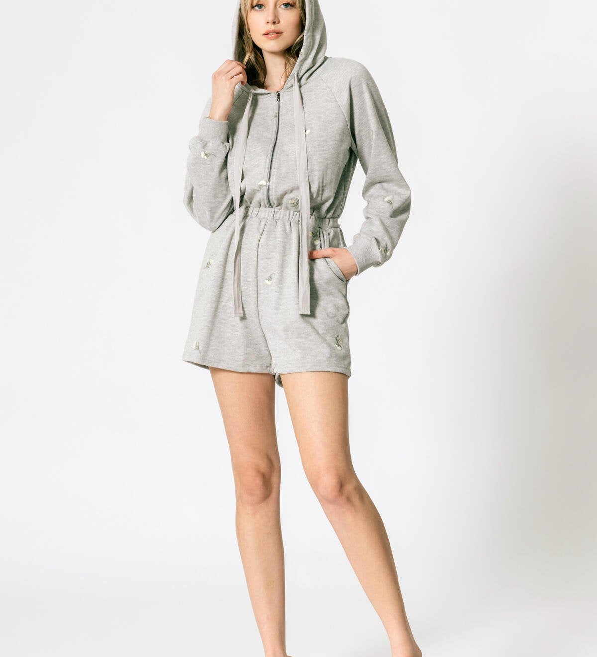 a model wearing a grey terry hooded romper against a white wall. 