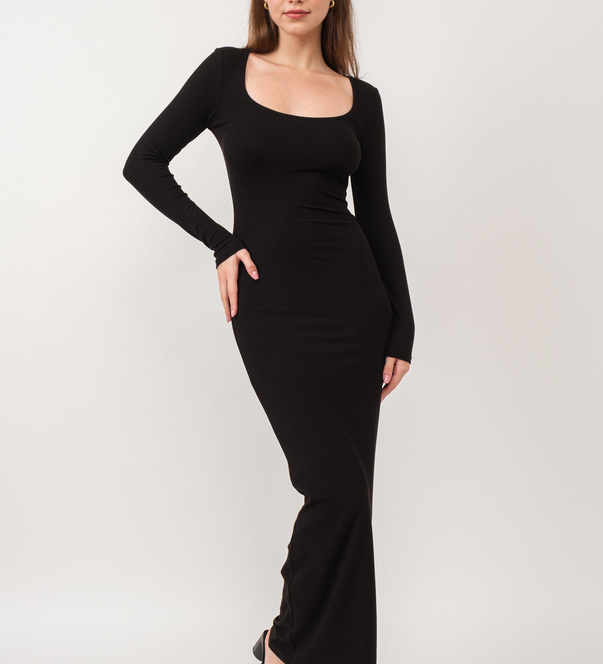 A model wearing a black ribbed maxi dress against a white wall.