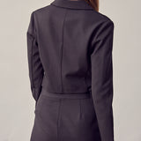 A model wearing a black double breasted cropped jacket backside view against a white wall. 