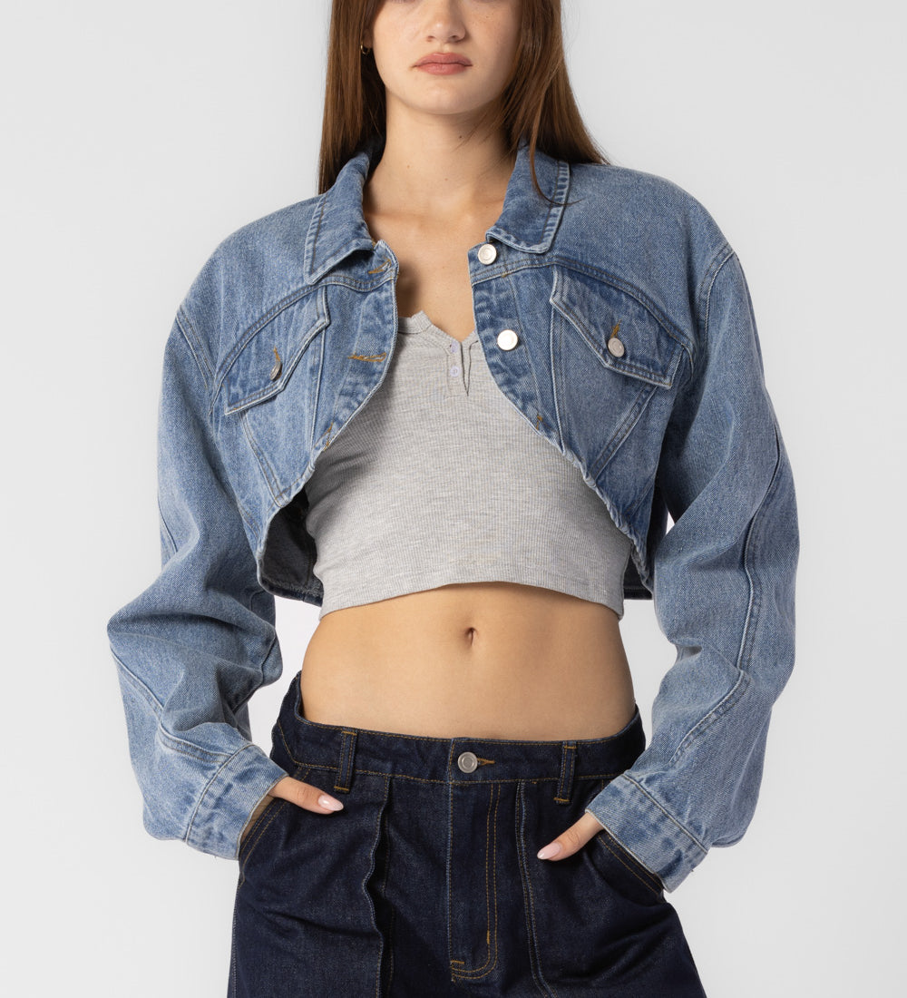 A model wearing a cropped denim jacket against a white wall. 